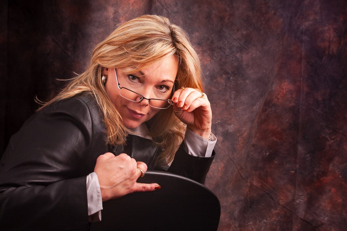 Terry Confident woman in a black leather jacket lowering her glasses during a personal portrait session.