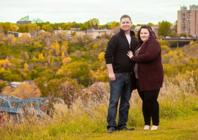 “Full-length engagement portrait of a couple with the Calgary city skyline in the background, captured by David Thielen Photographic Artistry”