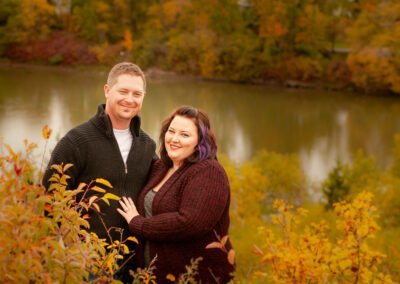 “Half-length engagement portrait of a couple standing lower on a hillside with the river and far shoreline forming the background, captured by David Thielen Photographic Artistry”