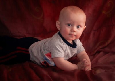 “Three-month-old baby lifts head and looks straight at the camera while sitting on a family quilt used for all their children’s milestone portraits, captured by David Thielen Photographic Artistry”