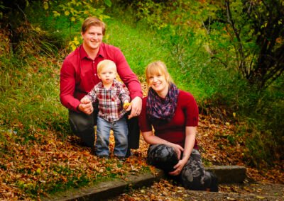 “Family sits together along a path in a park with green grass and shrubs in the background, captured by David Thielen Photographic Artistry”