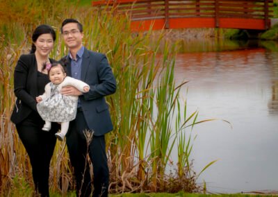 “Mother and father pose together holding their approximately six-month-old baby between them, captured by David Thielen Photographic Artistry”