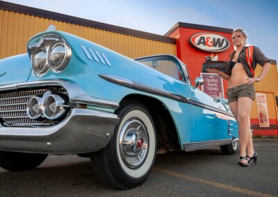 “Classic 1957 baby blue Chevrolet parked with an A&W sign in the background, featuring a car hop holding a tray, dressed in retro uniform, captured by David Thielen Photographic Artistry”