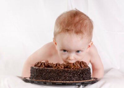 "A one-year-old child crouches over a chocolate cake, eyes wide with curiosity and excitement. Just moments away from diving headfirst into his first-ever taste of chocolate, his expression says it all: 'Can I really do this?'"