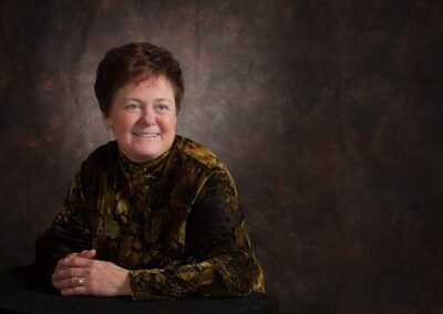 “Single woman poses in a formal low-key studio portrait, wearing a dark dress against a dark background, positioned on the left side of the frame looking into the image, captured by David Thielen Photographic Artistry”