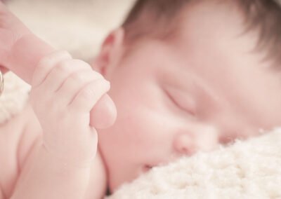 Alt Text “Newborn baby sleeps peacefully while grasping mother’s hand, capturing a tender early-motherhood moment, photographed by David Thielen Photographic Artistry”
