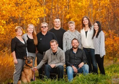 “Parents pose with their adult children and spouses in their backyard during fall, surrounded by autumn colors, captured by David Thielen Photographic Artistry”