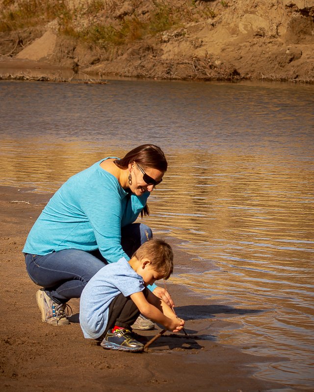 Moments-of-Wonder-at-the Waters-Edge” A mother and her young son play in the sand at Writing-On-Stone Provincial Park. This authentic motherhood photography session captures their deep connection.”